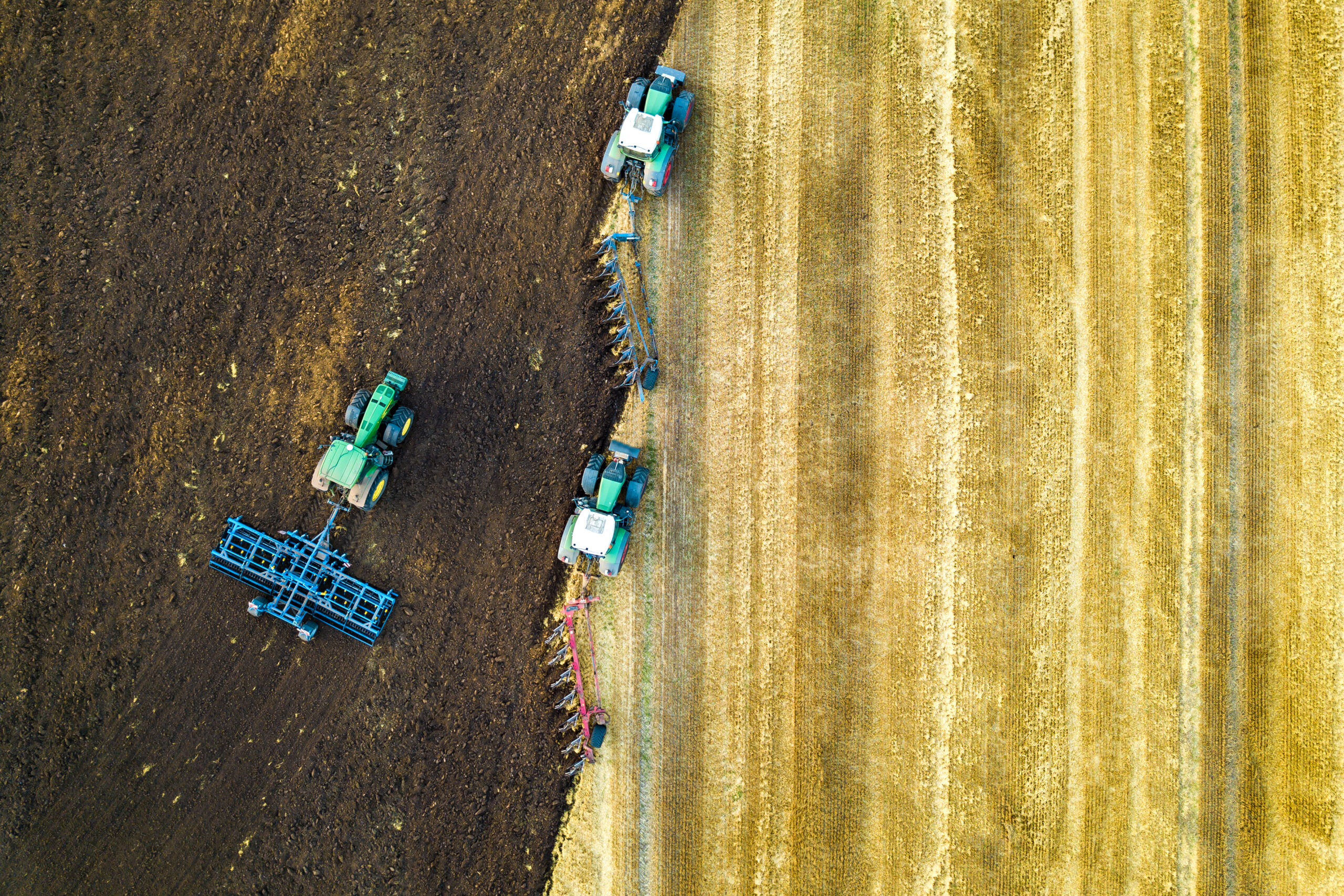 Aerial view of a tractor plowing black agriculture farm field after harvesting in late autumn.
